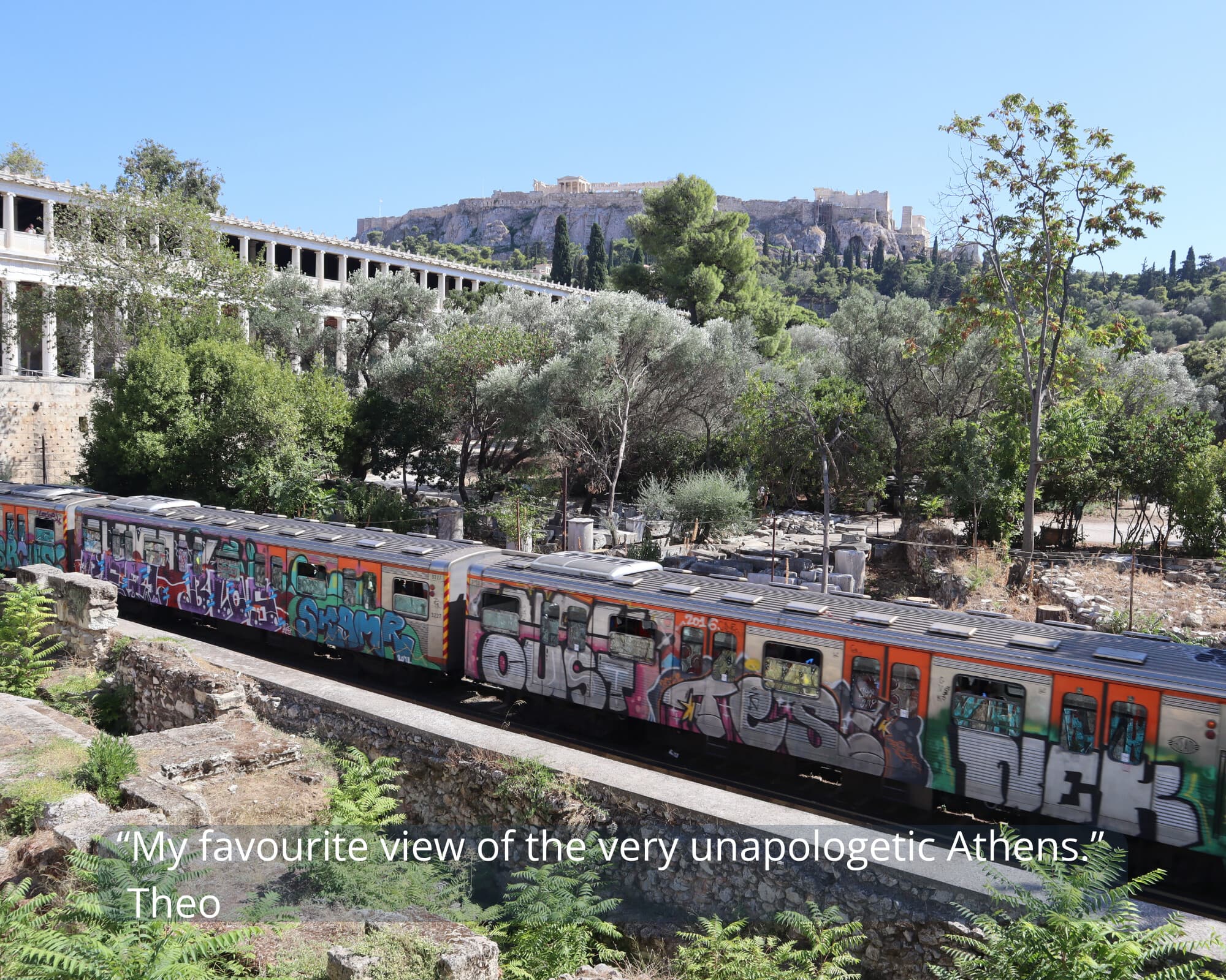 A graffiti-covered Athens metro train passing below the Acropolis - Monobrow Holidays Greece